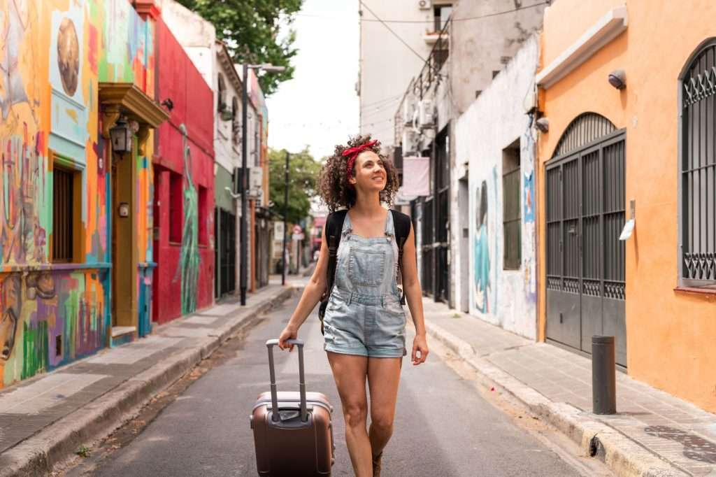 A traveling woman with her luggage walking a colorful street_PhenomenalMomentsTravel